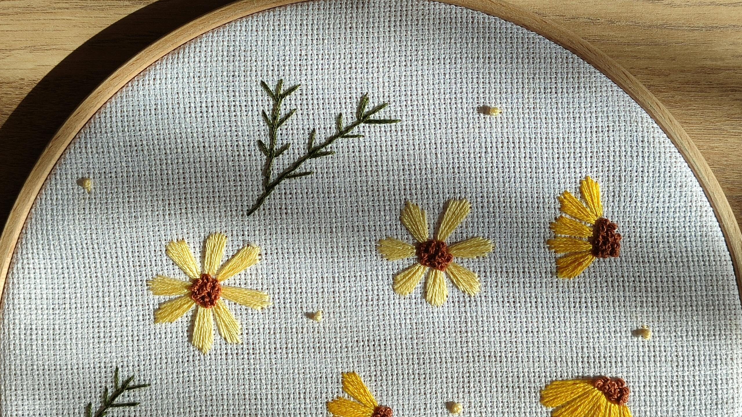 Beautiful embroidery of yellow flowers on canvas, framed in a wooden hoop with natural light.