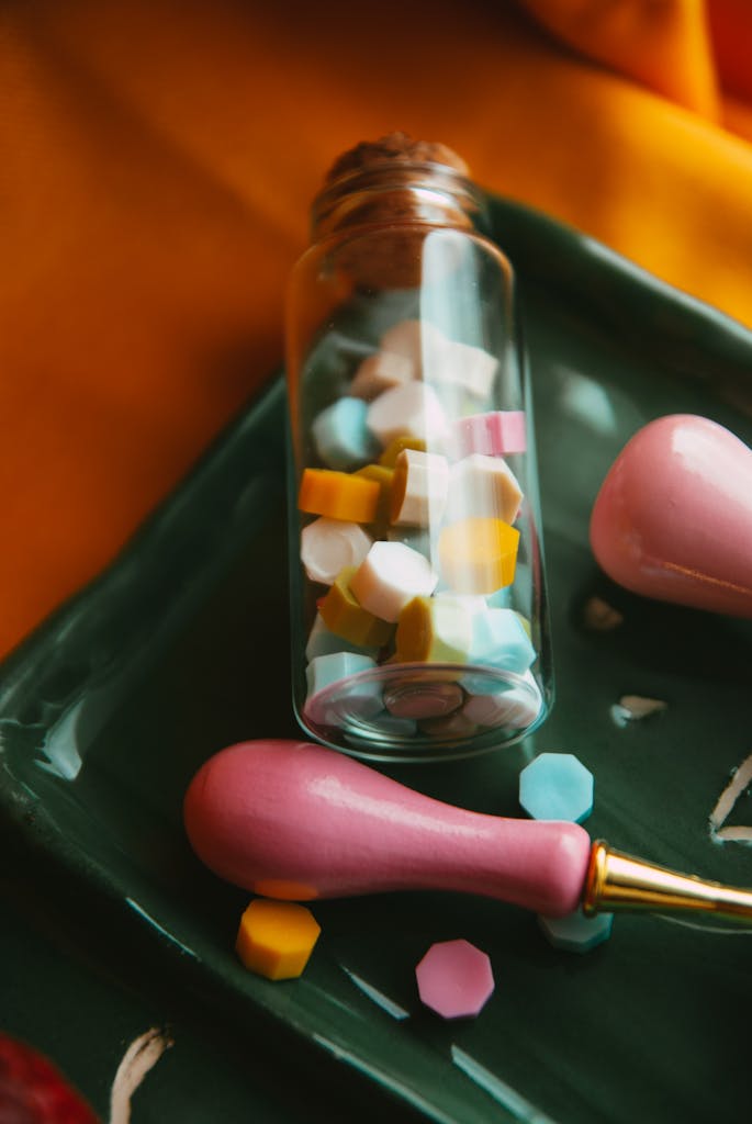 Close-up of colorful octagonal candies or pills in a glass vial on a green tray.