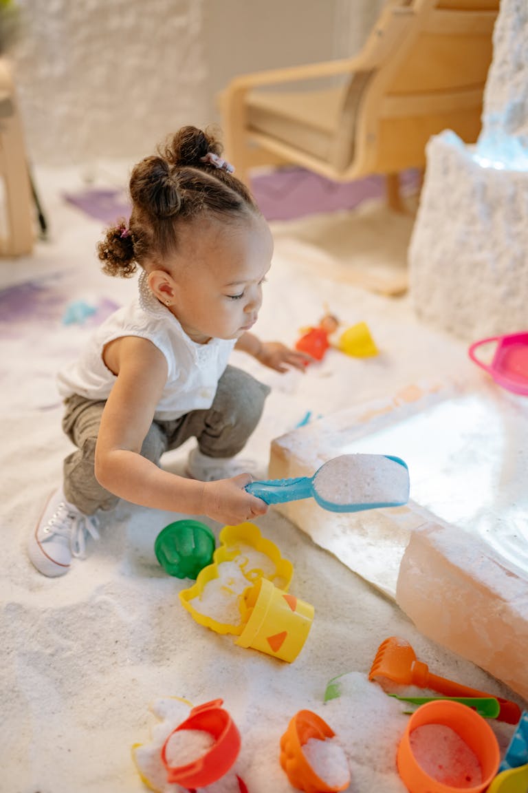 Young girl playing with toys in salt, exploring sensory activities indoors.